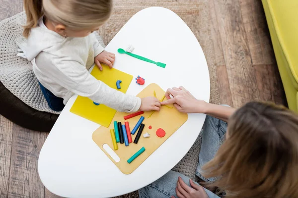 Overhead view of mom pointing at plasticine near daughter at home — стоковое фото