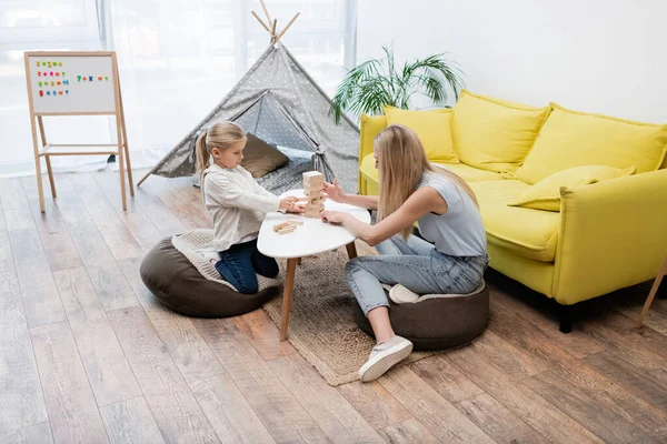 Kid and mother playing wood blocks game on coffee table at home — стокове фото