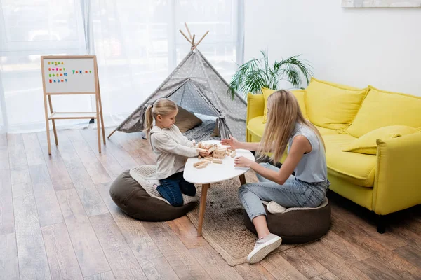 Child and mother playing wood blocks game near couch and teepee at home — Foto stock