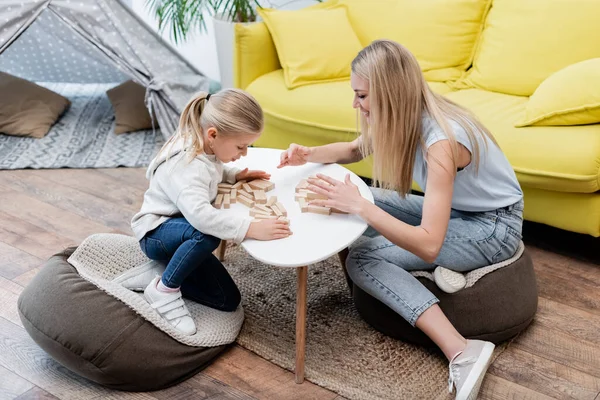 Side view of smiling family sitting near wooden blocks on coffee table at home — Photo de stock