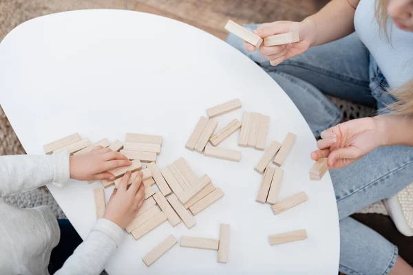 Cropped view of mother holding wooden blocks near kid and coffee table at home — стоковое фото