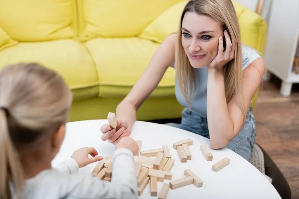 Smiling woman holding wood block while playing with child at home — стоковое фото