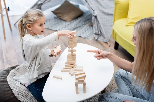 Blurred woman pointing at wood blocks game while child playing near coffee table — Foto stock