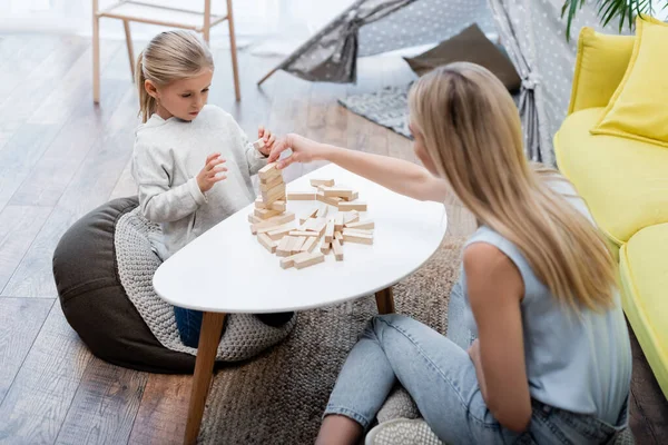 Parent and kid playing wood blocks game on coffee table near couch at home — Stock Photo