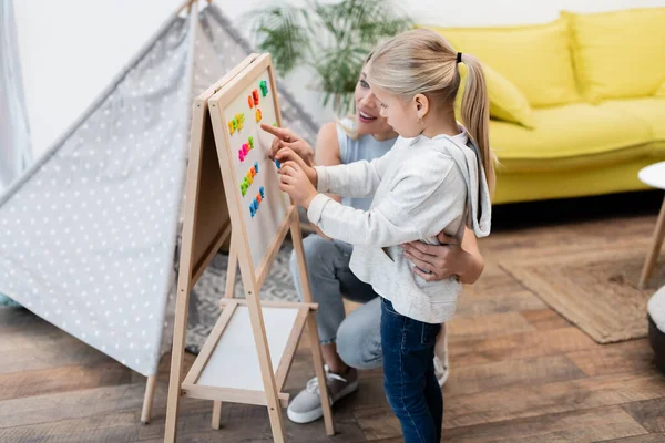 Parent hugging child and pointing at magnetic easel at home — стоковое фото