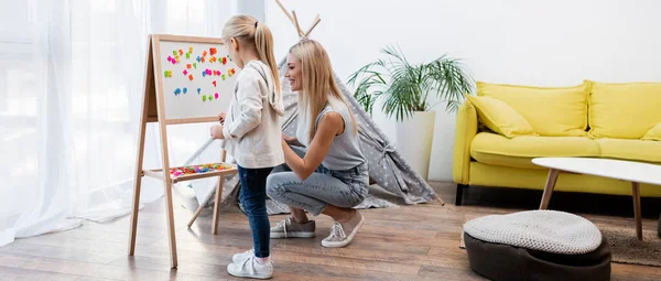 Parent and girl standing near magnetic easel at home, banner — Stockfoto