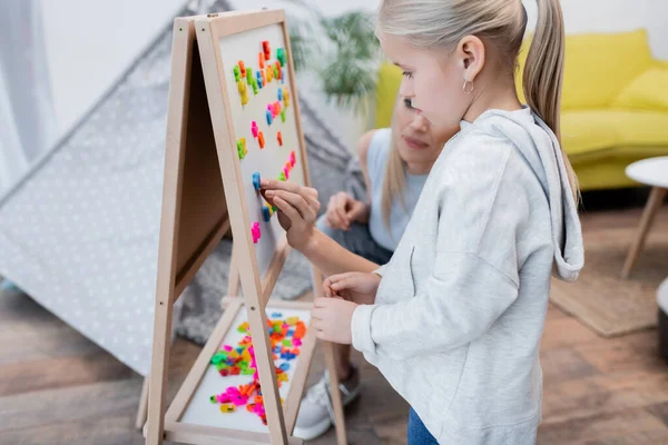 Kid standing near mom putting magnets on easel at home — Fotografia de Stock