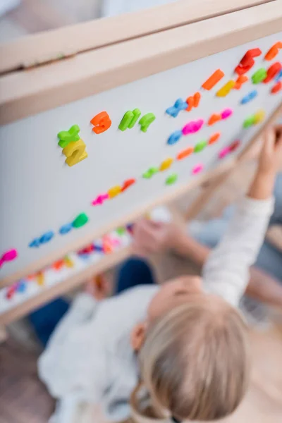 Overhead view of colorful magnets on easel near kid at home — Stock Photo