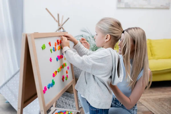 Child fastening colorful magnets on easel near parent at home - foto de stock