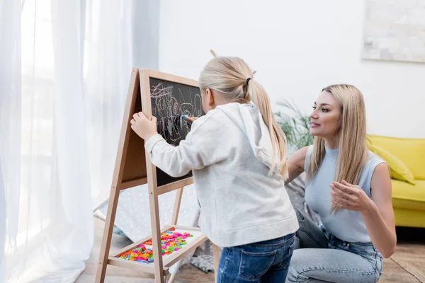 Kid drawing on chalkboard near parent at home — Stock Photo