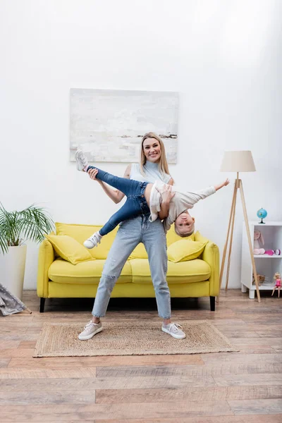 Smiling mom lifting daughter and looking at camera at home — Photo de stock