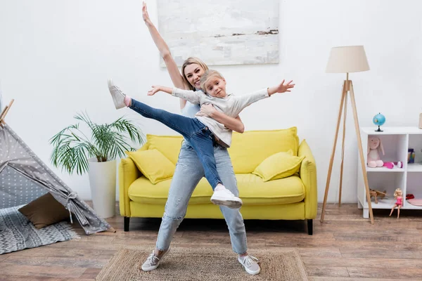 Happy woman holding child near couch and teepee at home — стоковое фото