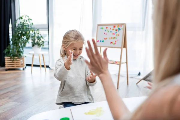 Blurred woman near smiling kid with paint on hands at home — Stock Photo