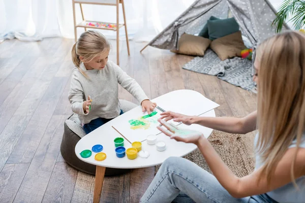 High angle view of woman and kid applying paint on hands at home — Stock Photo