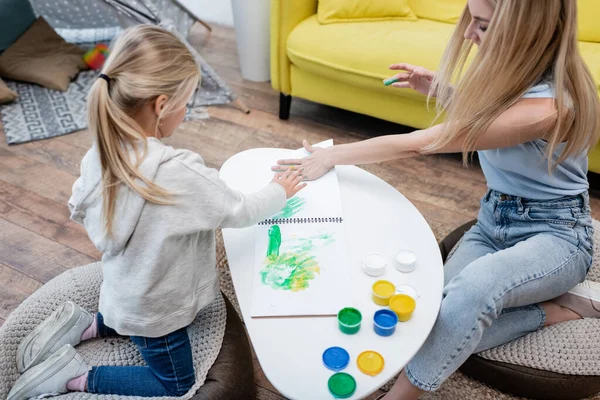 Mom and kid applying paint on sketchbook at home — стокове фото