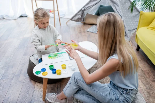 Kid applying paint on hand near mom in living room — стоковое фото