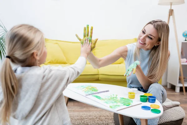 Smiling woman and kid with paint on hands giving high five at home — Photo de stock