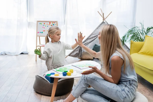 Positive woman and child giving high five while painting at home — стоковое фото