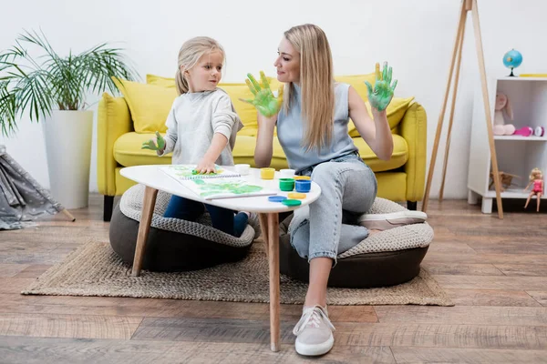 Kid with paint on hands looking at mother near coffee table at home — Photo de stock