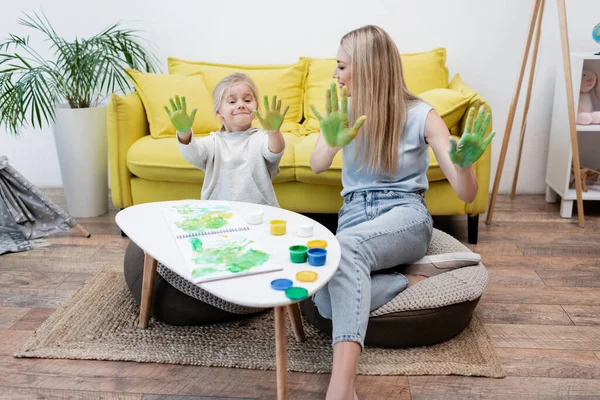 Happy child and mother showing hands in paint at home — стоковое фото