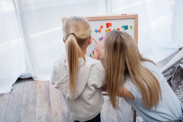 Back view of woman pointing at magnetic easel near kid at home — Fotografia de Stock