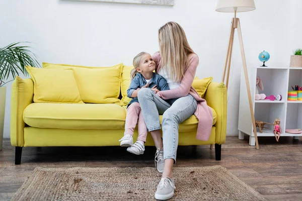 Parent hugging smiling daughter on couch at home — Stock Photo