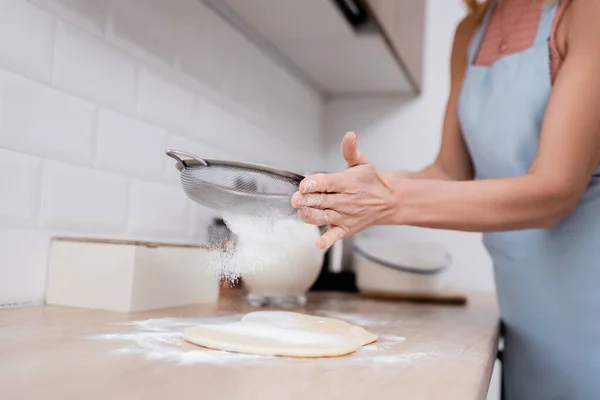 Обрізаний вид зрілої жінки, що поливає борошно на тісто на кухні — стокове фото