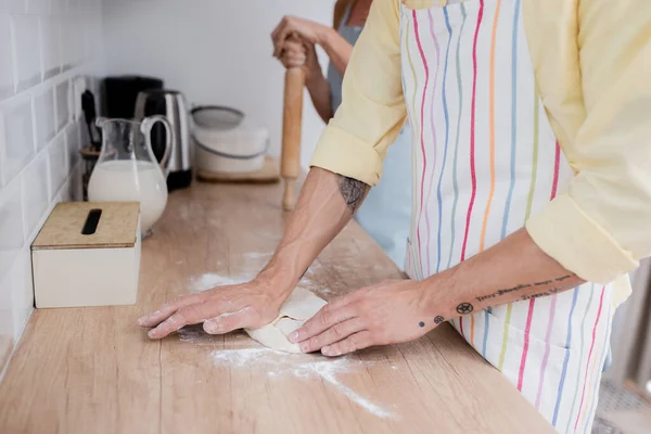 Vista recortada del hombre maduro preparando la masa cerca de la esposa borrosa con rodillo y leche en la cocina - foto de stock