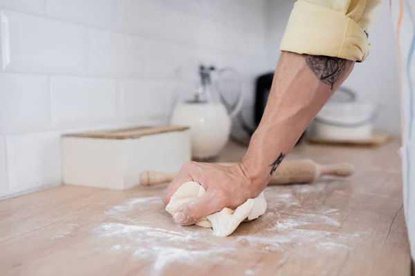Cropped view of tattooed man preparing dough near rolling pin in kitchen — Stock Photo