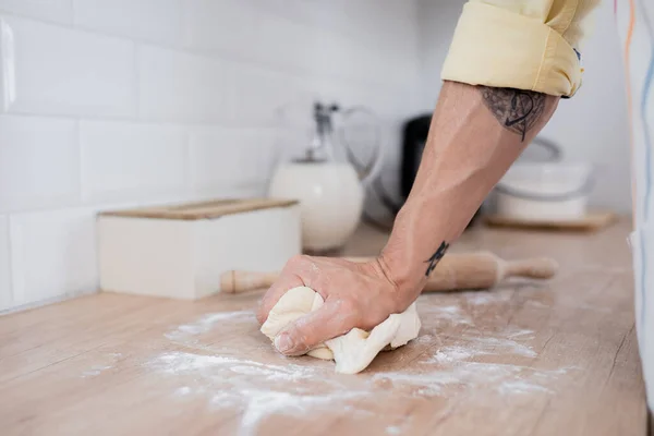 Cropped view of tattooed man preparing dough near rolling pin in kitchen — Stock Photo