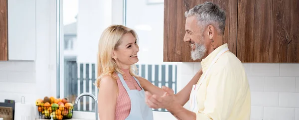 Positif mature homme parler à femme dans tablier dans la cuisine, bannière — Photo de stock