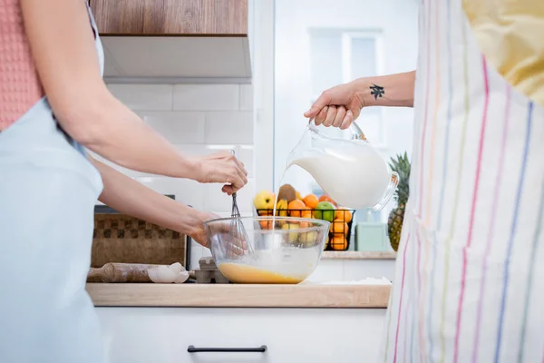 Ausgeschnittene Ansicht eines verschwommenen Mannes, der Milch in Schüssel gießt, während seine Frau in der Küche Eier mischt — Stockfoto