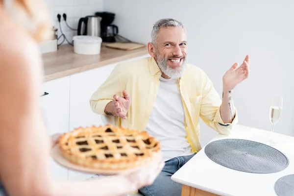 Позитивный мужчина средних лет смотрит на размытую жену с домашним пирогом — стоковое фото