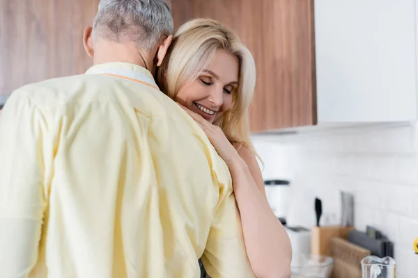 Улыбающаяся женщина обнимает зрелого мужа на кухне — стоковое фото