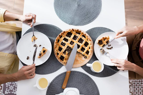 Vue du dessus du couple mature coupant la tarte près du thé sur la table de cuisine — Photo de stock