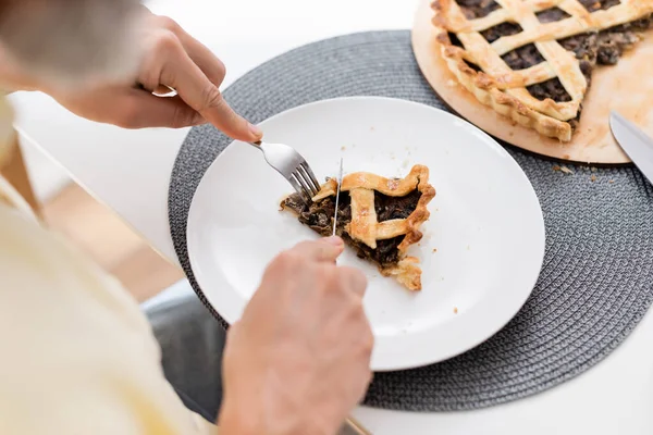 Vista cortada de homem desfocado cortando torta saborosa na placa na cozinha — Fotografia de Stock