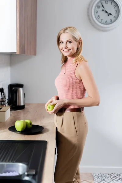 Sorridente donna matura in possesso di mela in cucina — Foto stock