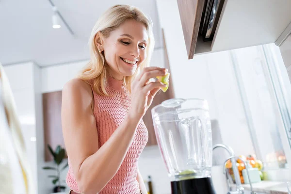 Allegro donna matura versando frutta in frullatore in cucina — Foto stock