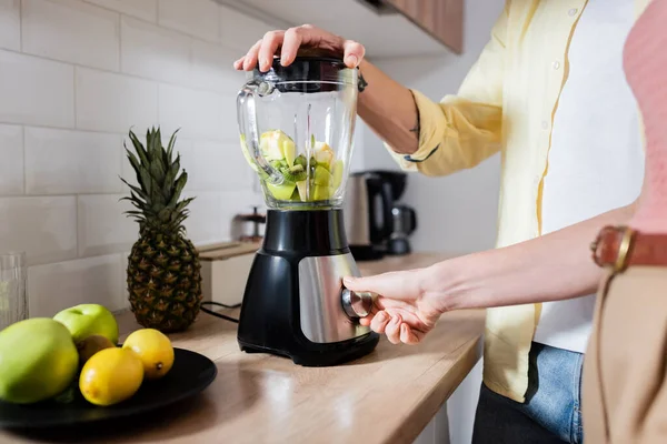 Cropped view of woman switching blender with fruits near husband in kitchen — Stock Photo