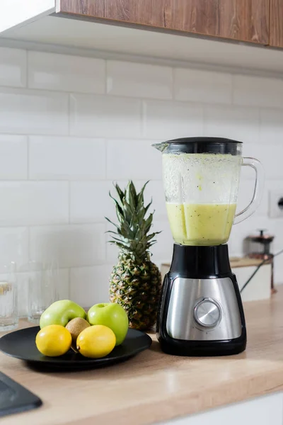 Fresh fruits near blender with smoothie in kitchen — Stock Photo