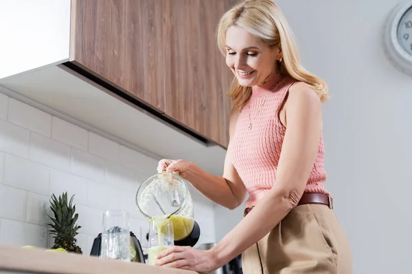 Lächelnde reife Frau gießt Frucht-Smoothie in Küche — Stockfoto