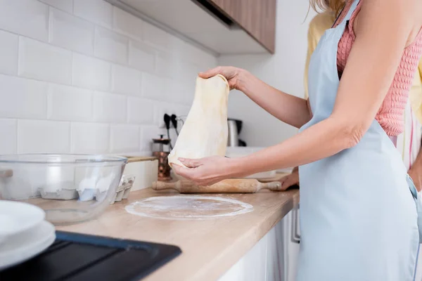 Vista recortada de la mujer en delantal sosteniendo la masa cerca del marido en la cocina — Stock Photo