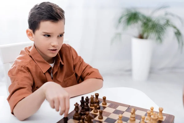 Thoughtful boy playing chess at home while sitting at table — Stock Photo