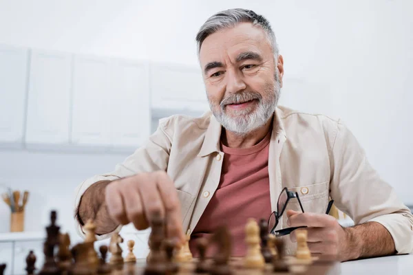 Smiling senior man playing chess in kitchen at home — Stock Photo