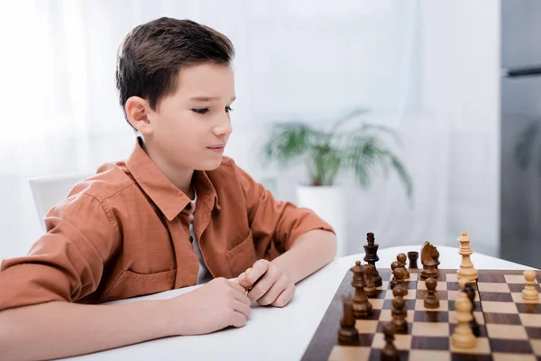 Niño jugando ajedrez mientras está sentado en la mesa en casa - foto de stock