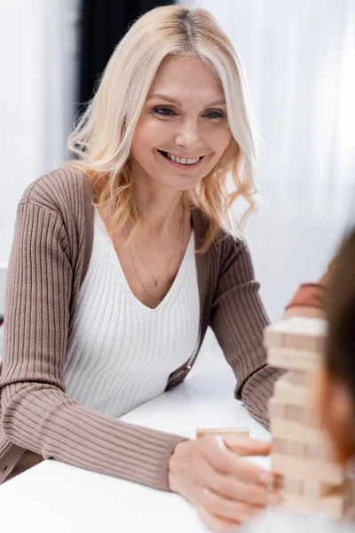 Blonde middle aged woman smiling near wood blocks game and blurred grandchildren — Stock Photo