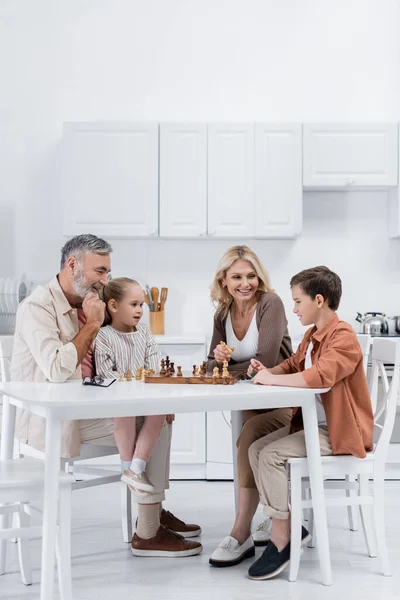 Heureux grands-parents jouer aux échecs avec les enfants dans la cuisine — Photo de stock