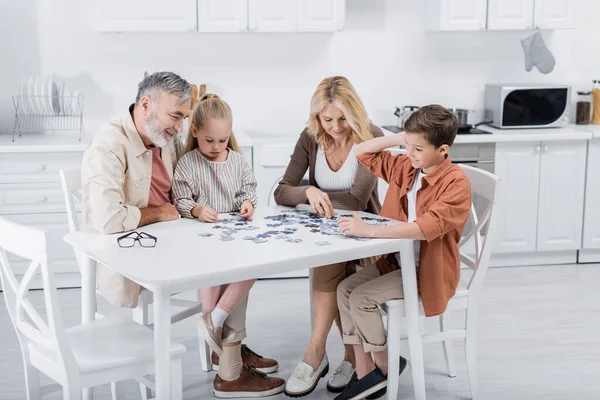 Діти з бабусею і дідусем грають в головоломку на кухонному столі — стокове фото