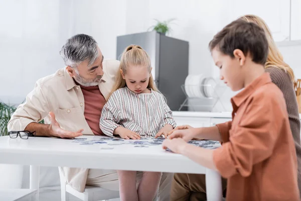 Niños jugando rompecabezas juego con los abuelos en la cocina - foto de stock