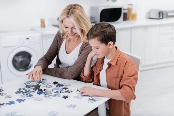 Happy middle aged woman with grandson playing jigsaw game in kitchen — Stock Photo
